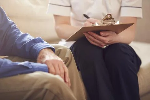 Close Up Of Female Doctor Making Notes During Home Visit To Senior Man For Stock Photos