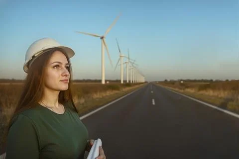 Close-up female engineer in hard hat holding plan on road, strong turbine p.. Stock Photos