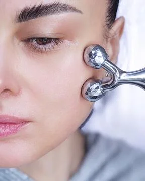 Close up of female face using a 3D silver massage roller on her cheek. Dail.. Stock Photos