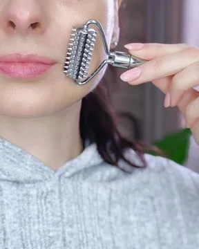 Close up of female face using a textured metal facial massage roller on her.. Stock Photos