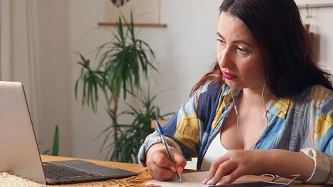 Close-up of a female freelancer making notes on paper while looking at a laptop. Stock Footage 170117952