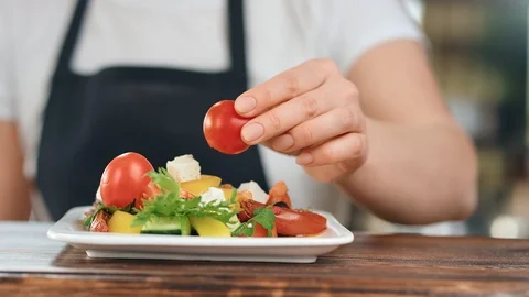 Close up female hand in apron adding fresh tomato to vegetable mix. Wide shot on Stock-Footage 124154974