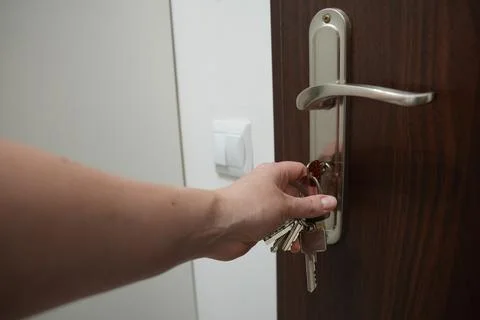 Close up of female hand inserting key into wooden door lock at home Stock Photos