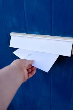 Close-up of a female hand inserting white envelopes into a letterbox door. Stock Photos