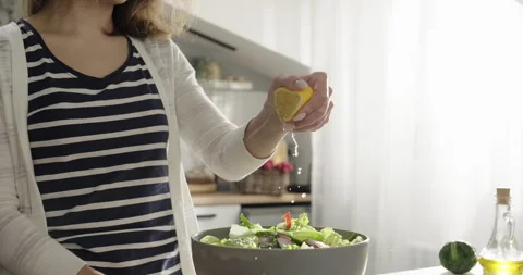 Close-up female hand squeezing fresh lemon juice on lettuce salad. Cooking Stock Footage 275731704