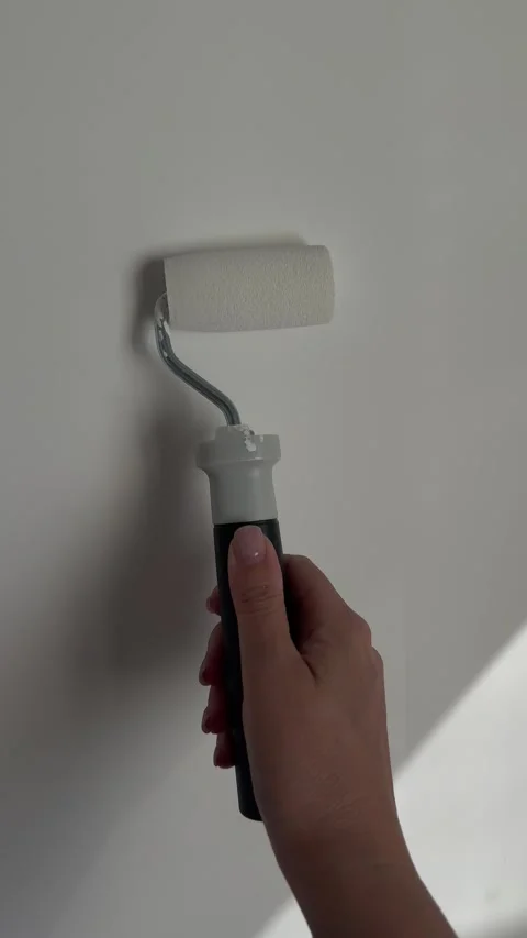 Close up of female hand using paint roller to paint smooth white interior wall d Stock Footage 335792462