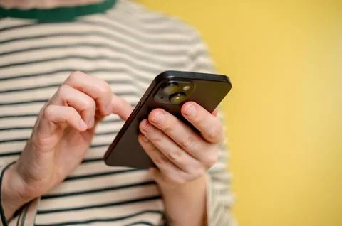 Close-up of female hand using smartphone isolated on yellow background. Stock Photos