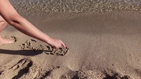 Close up of female hand writing word Summer with finger on sand at beach Stock Footage 213902204
