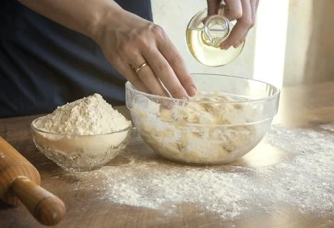 Close-up of female hands adding oil to the dough, on the background of flour and Photos