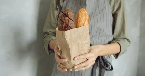 Close up of female hands of a baker or seller in uniform holding tasty baguettes Stock Footage 128979853