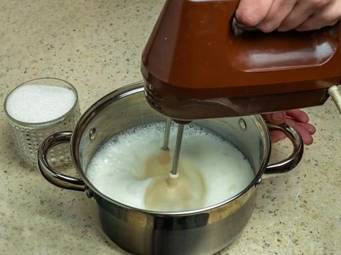 Close-up female hands beating raw egg whites in stainless steel saucepan with Stock Photos