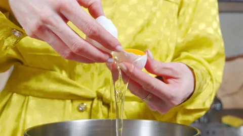 Close-up of female hands breaking eggshells and dividing yolks and whites into Stock Footage 182952950