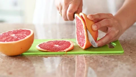 Close-up of female hands carefully slicing fresh ripe grapefruit into thin .. Video stock 314385151