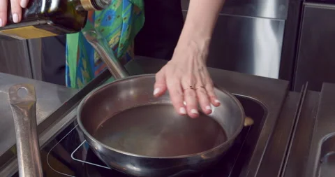 Close up of female hands checking temperature of frying pan and pouring olive Stock Footage 154479609