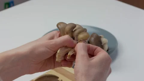 Close-up of female hands on a chopping board separating fresh mushrooms into Stock Footage 193380320