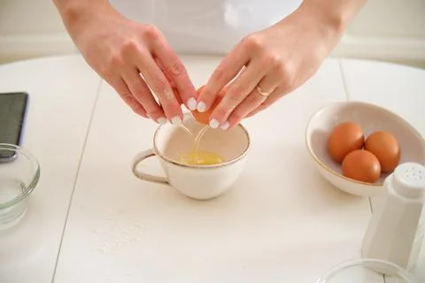 Close-up of female hands cracking egg into bowl on kitchen table. Process o.. 스톡 사진