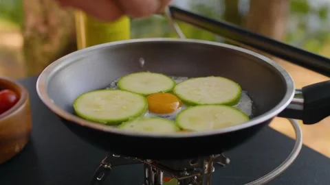 Close-up of female hands cracking a quail egg into a frying pan at the campsite. Video stock 290388037