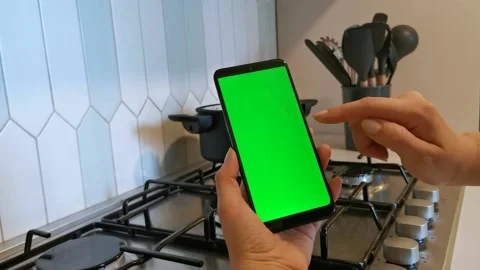 Close up female hands hold mobile phone with green screen, modern kithen on Stock Footage 201863993