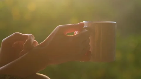 Close-up female hands holding a cup of hot coffee to drink at sunrise outdoors. Видео 244096448