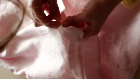 Close up of female hands manually sews button to pink linen fabric using needle. Video stock 316920523