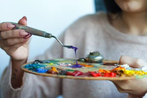 Close-up of female hands mixing paints on a palette with a spatula against a  Stock Photos