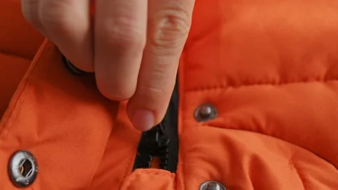 Close-up of female hands open black lock on winter orange jacket, down jacket Stockbeeldmateriaal 220660455