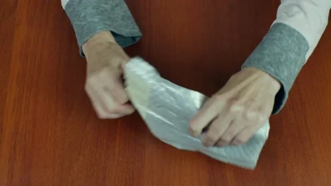 Close-up of female hands opening a small parcel in a plastic package and taking Stockbeeldmateriaal 220470017