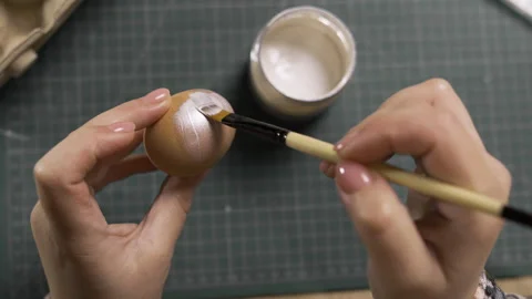 Close-up of female hands painting an Easter egg in silver color with brush Stock Footage 329090672