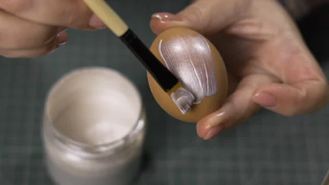 Close-up of female hands painting an Easter egg in silver color with brush Stock Footage 329090708