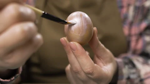 Close-up of female hands painting an Easter egg in silver color with brush Stock Footage 329090712