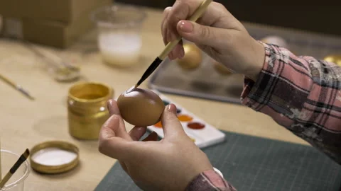 Close-up of female hands painting an Easter egg with a brush and silver paint Stock Footage 329090749