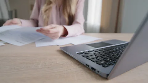 Close-up female hands with papers sorting documents typing on laptop at table in Video stock 169864464