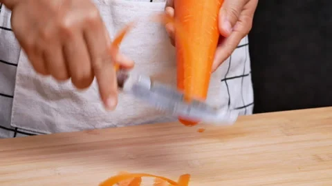 Close-up of female hands peeling fresh juicy carrot by peeler on cutting board. Stock Footage