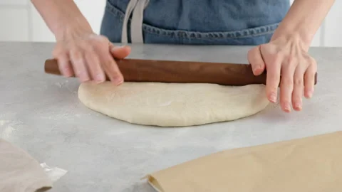 Close-up of female hands roll out the dough with a wooden rolling pin on a light Stock Footage 146140874