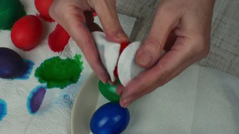 Close-up female hands rubbing multi-colored painted Easter eggs with vegetable Stock Footage 240598165