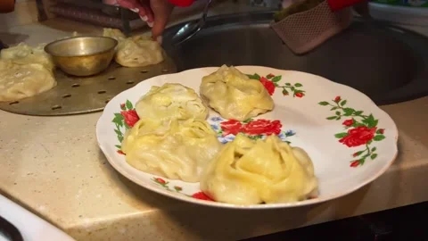 Close-up of female hands serving cooked manti dumplings onto a plate Stock Footage 330172724