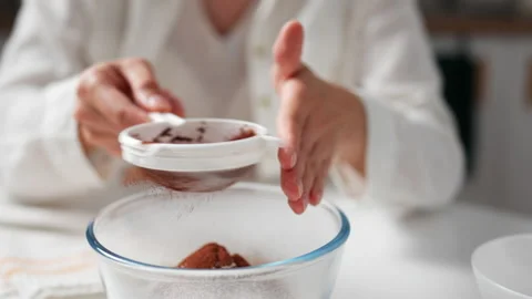 Close-up of female hands sifting cocoa powder with sieve into glass bowl. Pr Stock Footage 213319048