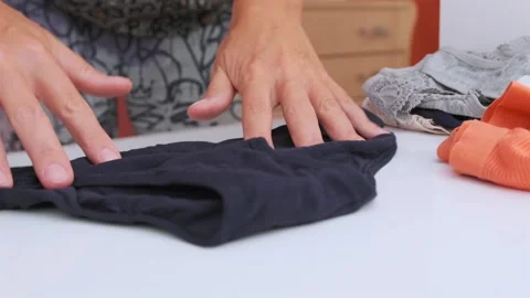 Close-up of female hands sorting and stacking freshly washed clothes on table Stock Footage 333769800