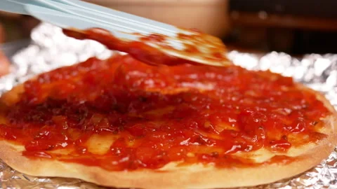 Close up of female hands spreading tomato sauce on pizza dough with a spatula. Stockbeeldmateriaal 158668953