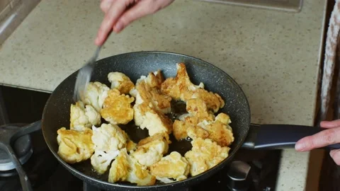 Close-up of female hands turning over pieces of fried cauliflower in a frying Stock Footage 220901070
