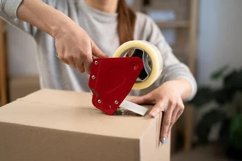 Close up of female hands using adhesive tape dispenser to seal cardboard box  Stock Photos