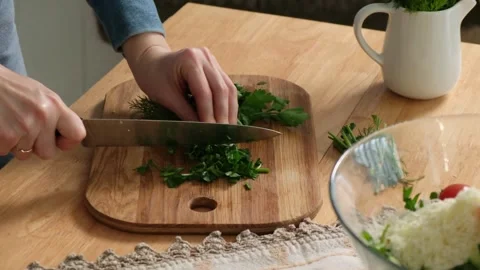 Close-up of female hands using a kitchen knife to chop fresh green parsley and Stock Footage 345048293