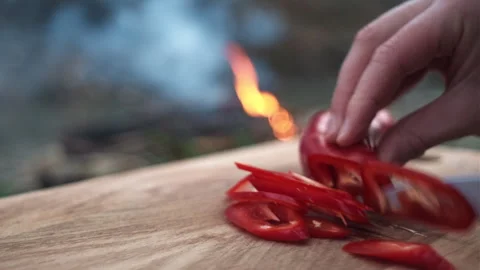 Close up of female hands using knife cutting fresh red pepper near bonfire Stock Footage 271546332