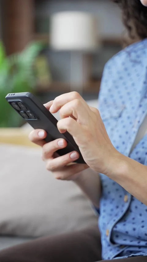 Close up of female hands using mobile phone in living room. Young woman engaged  Stock Footage 330658954