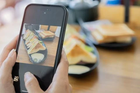 Close-up female hands using smart phone taking photo of sandwiches and coff.. Stock Photos