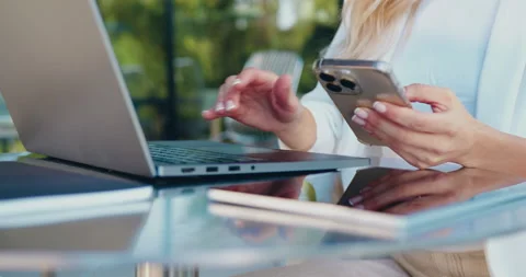 Close-up of a female hands using a smartphone and typing on a laptop while Stock Footage 348648809