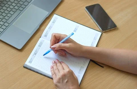 Close-up of female hands write in a notebook on a wooden table, a smartphone and Stock Photos
