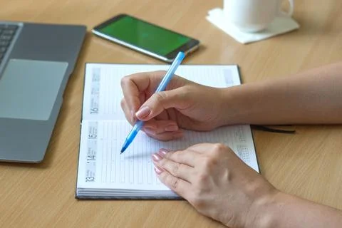 Close-up of female hands write in a notebook on a wooden table, a smartphone and Stock Photos