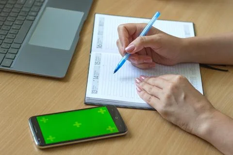 Close-up of female hands write in a notebook on a wooden table, a smartphone and Stock Photos