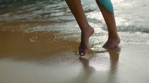 Close-up of female legs dancing and walking along the waves and sand of a beach Stock Footage